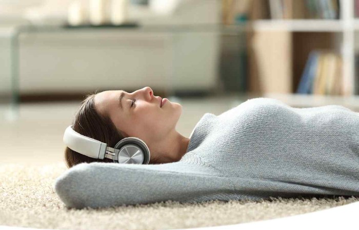 Femeie care mediteaza pe podea, cu castile pe urechi
