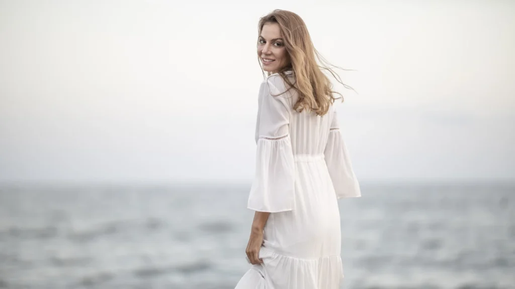 Femeie pe plajă, în haine confortabile, radiază energie feminină în peisajul mării